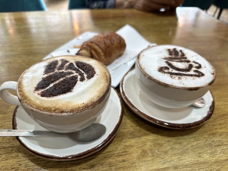 Cappuccino with chocolate-dusted latte art, served with a croissant